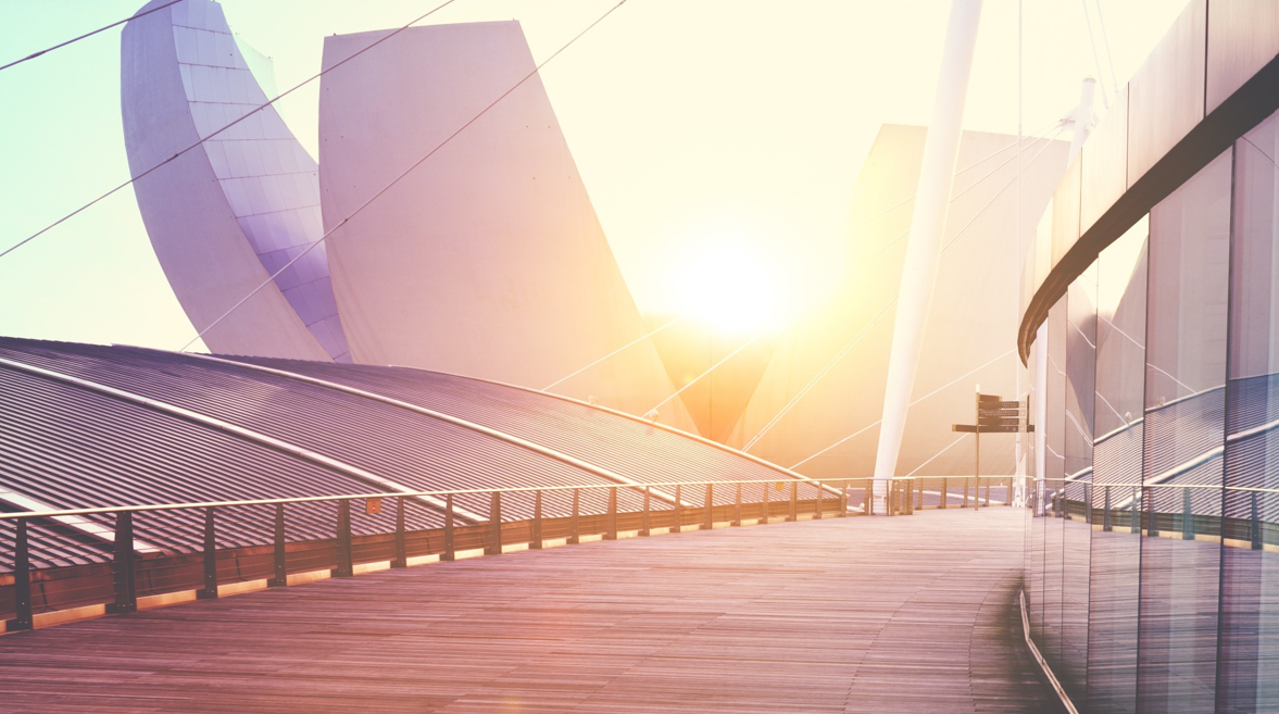 A curved walkway running between modern buildings at sunset, glass on one side and a sculptural roof on the other