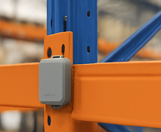 Ein Square-Impact-Sensor, an den Ständer eines orange-blauen Palettenregals geschraubt, auf Höhe eines Trägers, in einem Lagergang